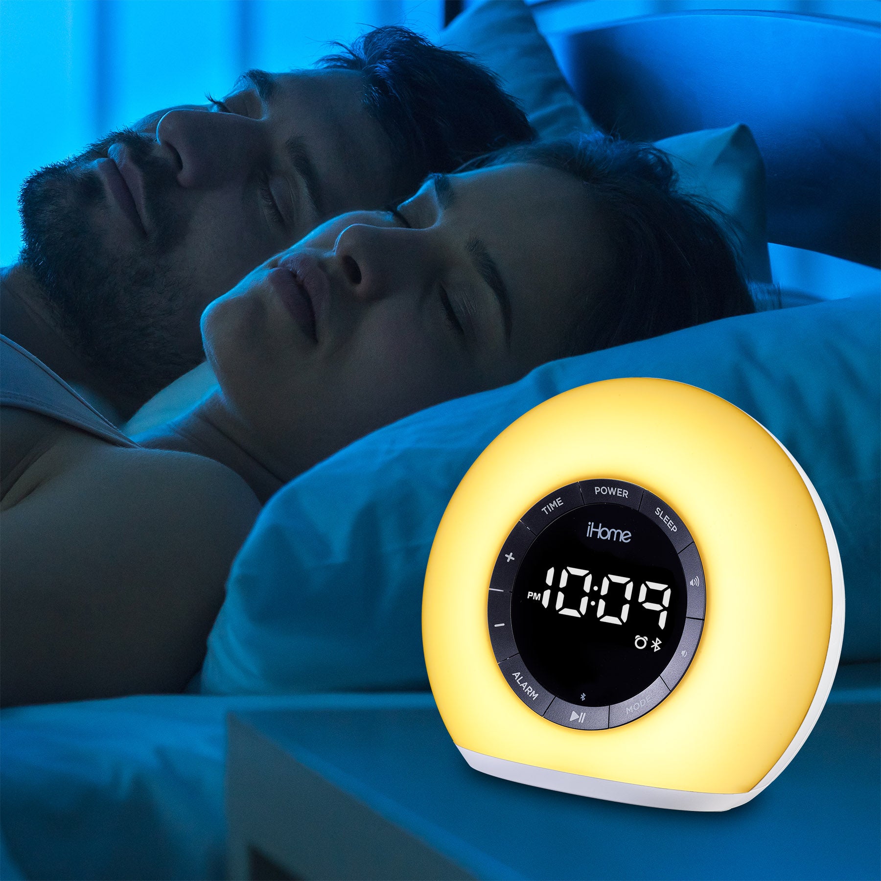 Couples sleeping peacefully with a Sunrise Alarm Clock Radio showing 10:09 and emitting a soft yellow light.