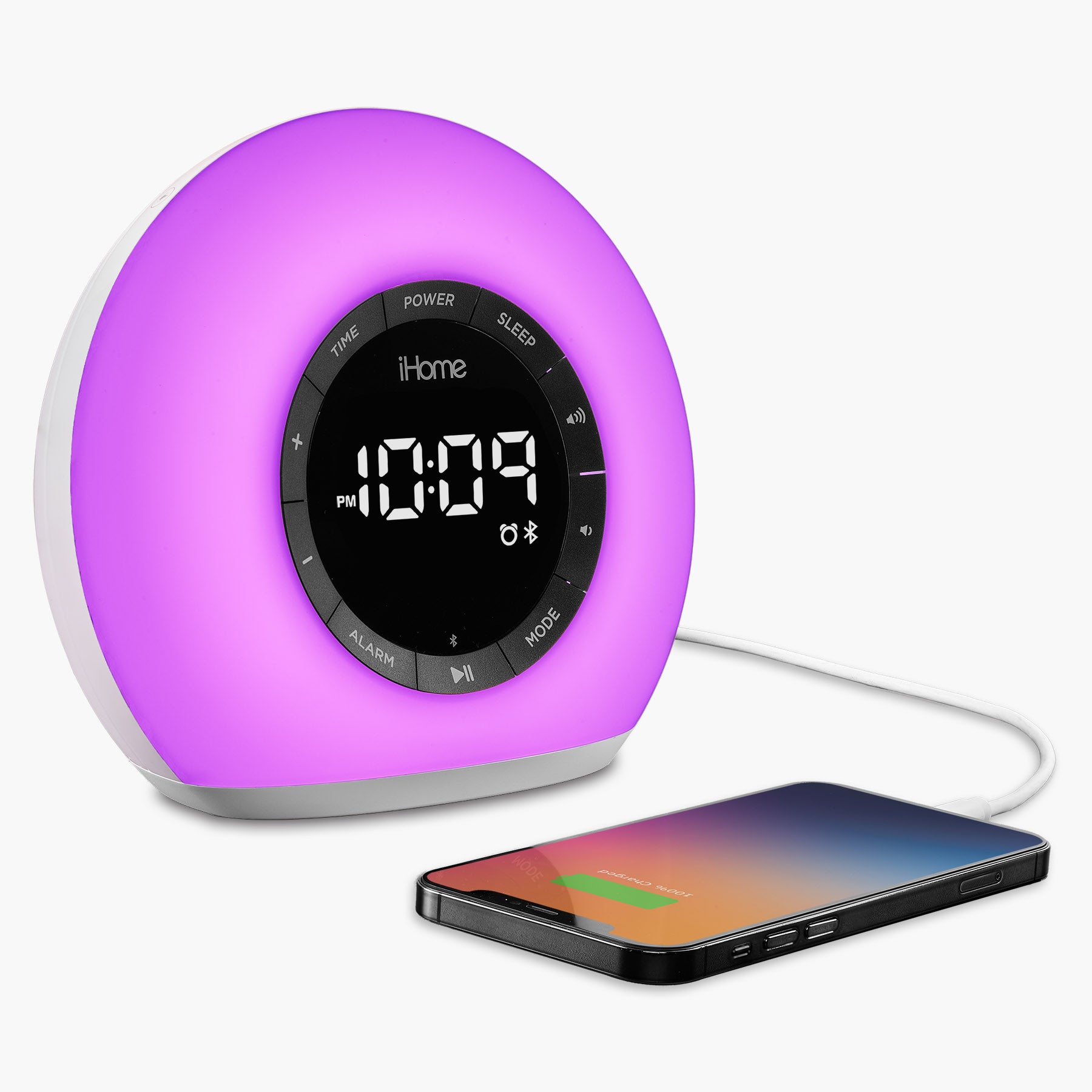 Sunrise alarm clock radio with Bluetooth speaker, color-changing LED lamp, and USB charging port next to a charging smartphone.